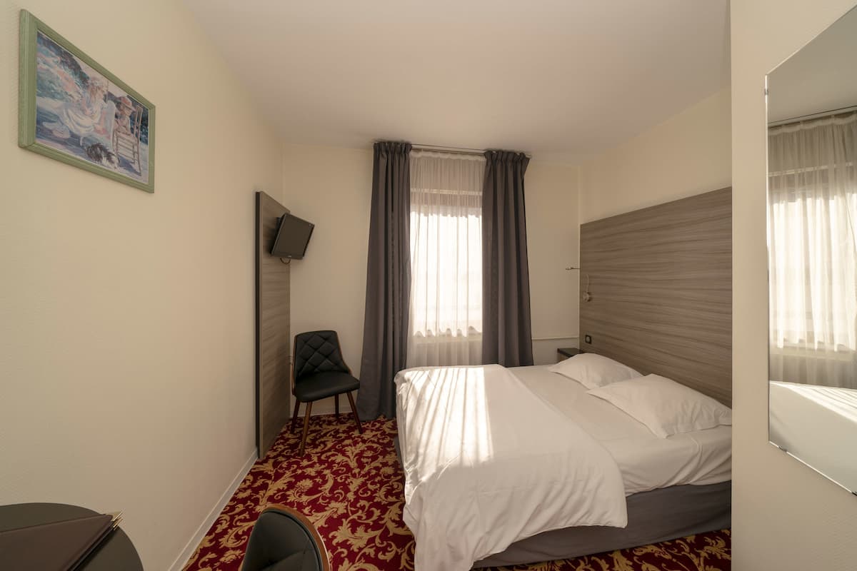 Une chambre d’hôtel avec un lit, une chaise, un bureau, une télévision et un tableau au mur.