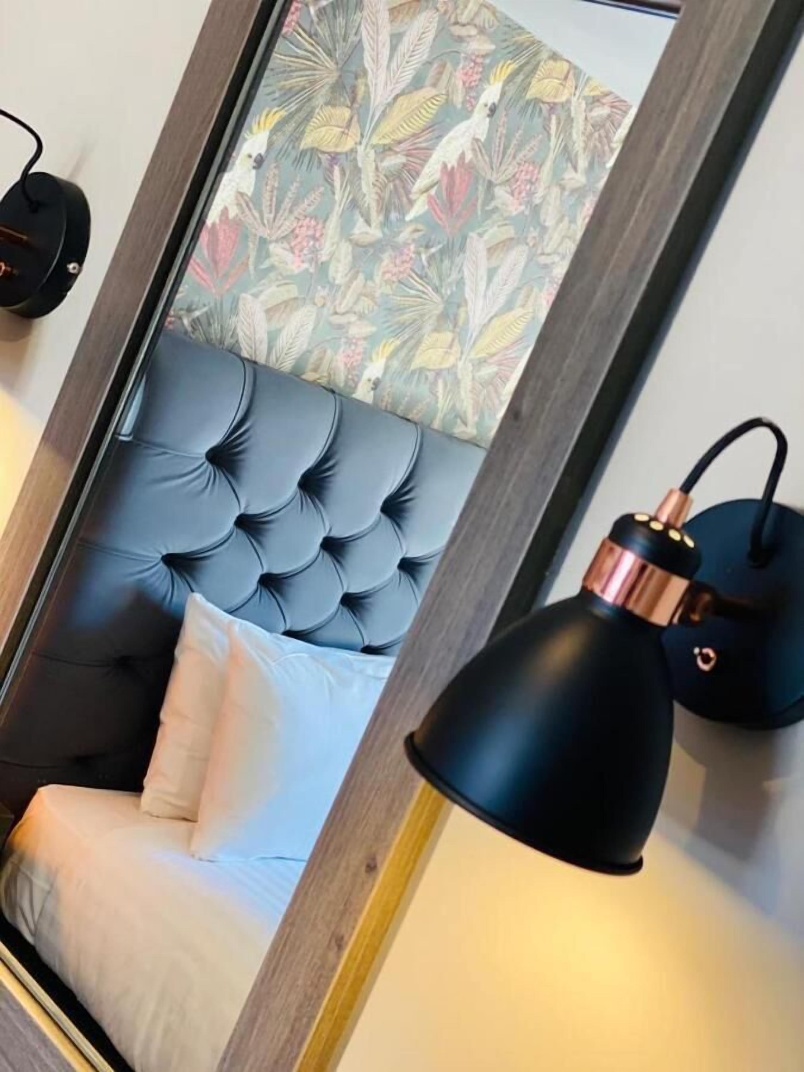 A bedroom with a tufted headboard, a white pillow, a black lamp, and a framed floral artwork on the wall.