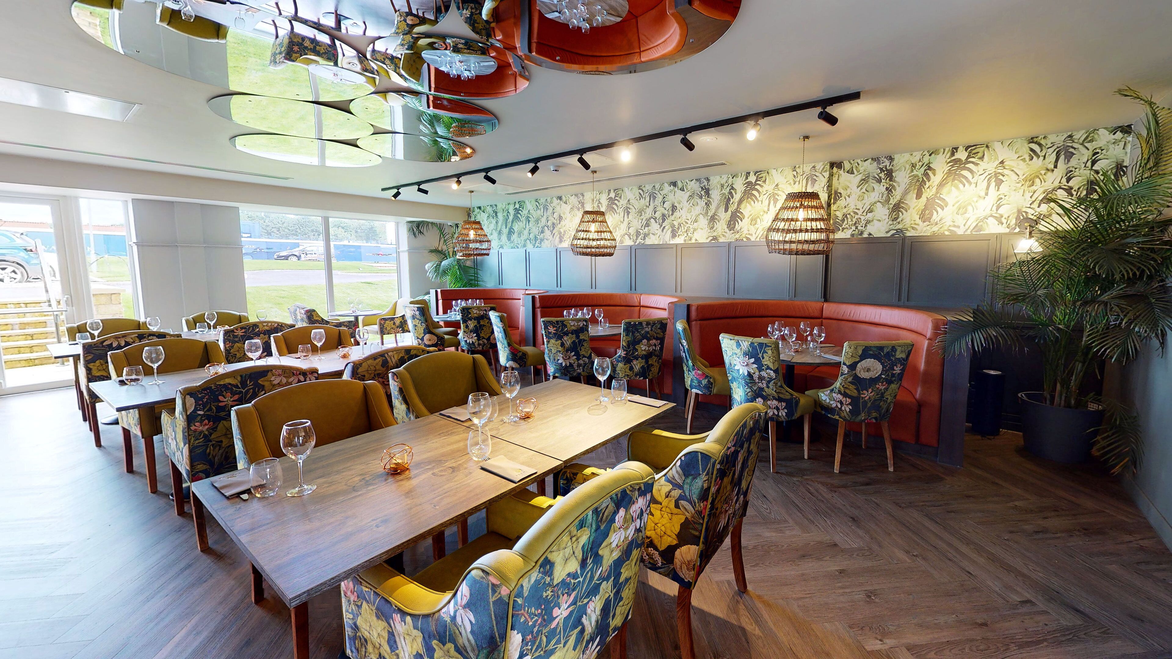 Ein Restaurant mit Holztischen, floralen Stühlen und Blick ins Freie.