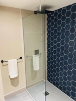 Un baño moderno con cabina de ducha de vidrio, pared color beige y salpicadero de azulejos hexagonales azul oscuro.