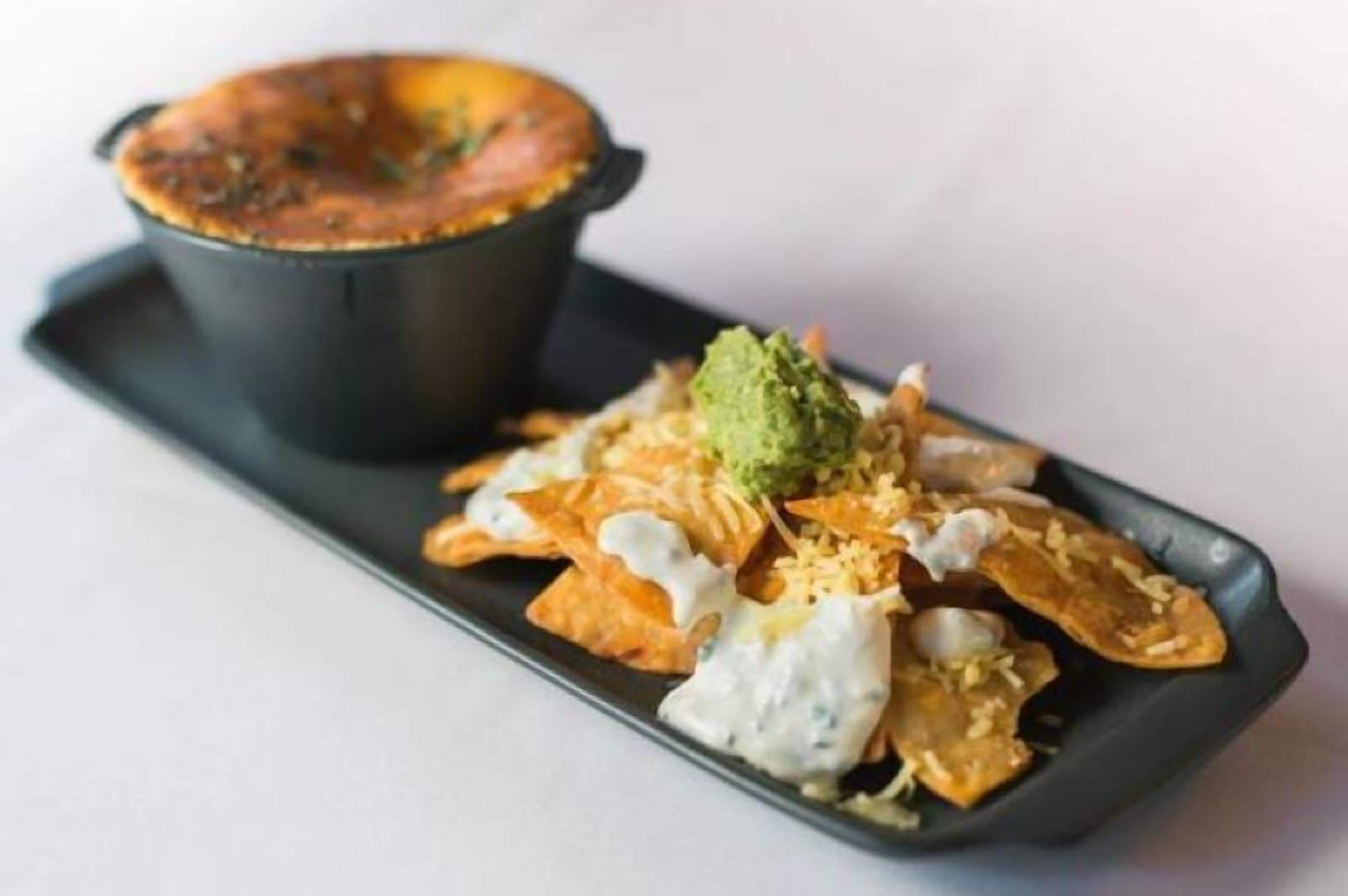 Un plat composé de nachos, de guacamole, de crème aigre et d’une pomme de terre au four.