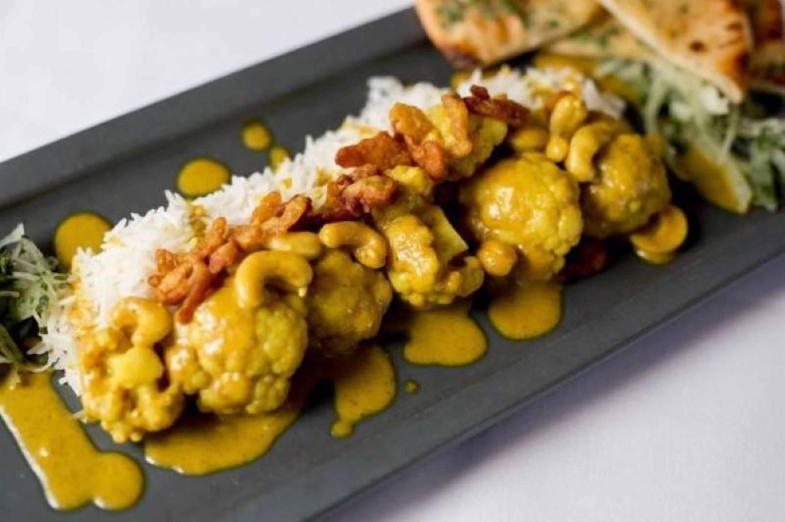 Un plato de comida con arroz, coliflor y salsa amarilla.