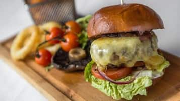 A burger with a toothpick on a wooden board, surrounded by cherry tomatoes and onion rings.