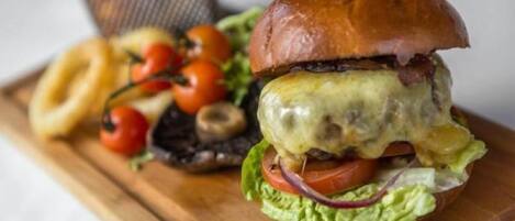 A burger with a toothpick on a wooden board, surrounded by cherry tomatoes and onion rings.