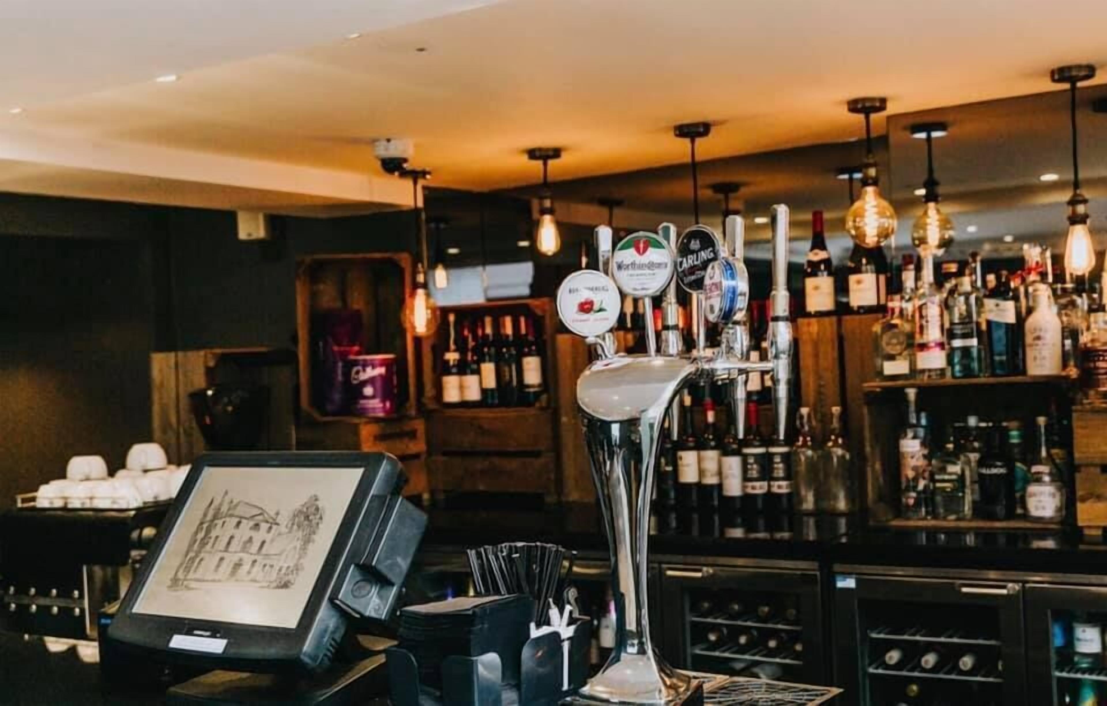 A bar area with a tap stand, shelves of bottles, and a framed picture on the counter.