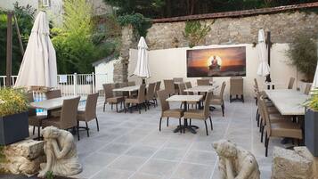 An outdoor patio with tables and chairs, a stone wall, and a Buddha statue.