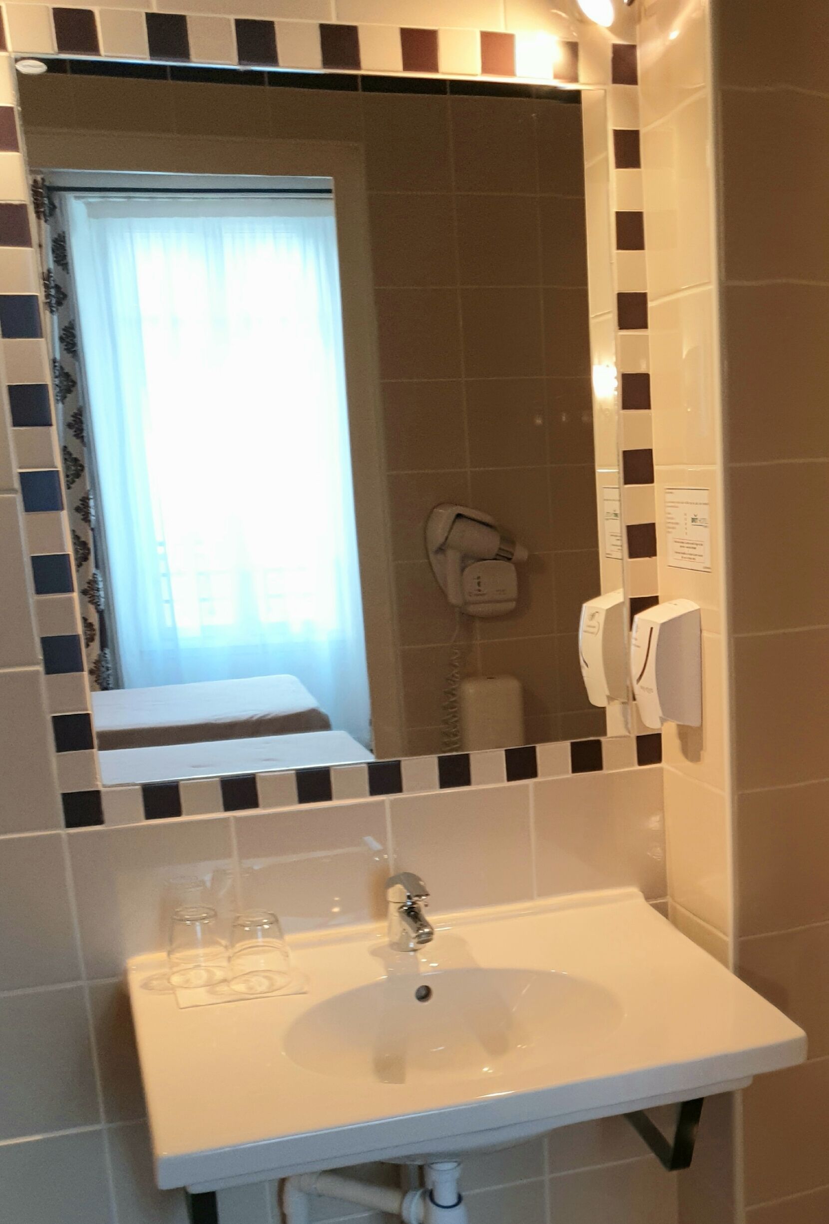 Un baño con un lavamanos blanco, un espejo y un secador de manos.