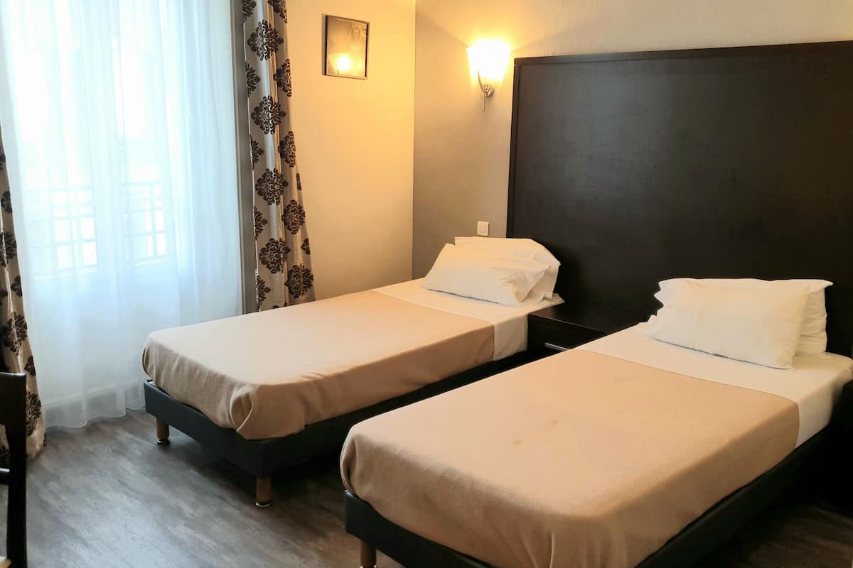Une chambre d’hôtel avec deux lits simples, un bureau, une chaise et une fenêtre avec des rideaux.