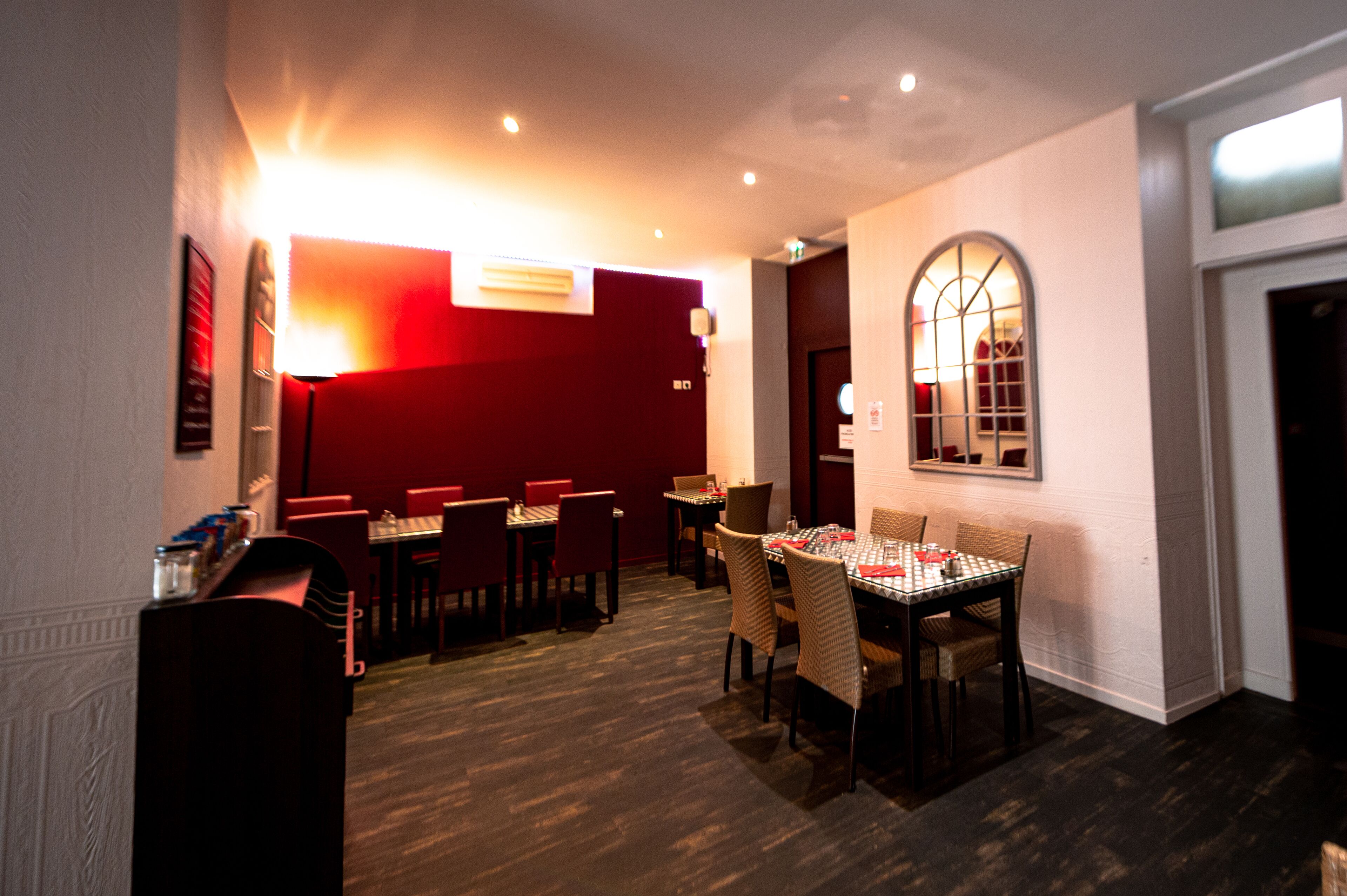 A restaurant with multiple tables and chairs, a red wall, and a window with a view.