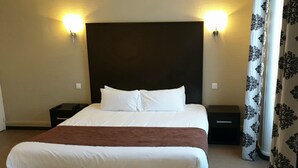 Une chambre d’hôtel avec un grand lit, deux tables de chevet et une tête de lit agrémentée de lampes fixées au mur.