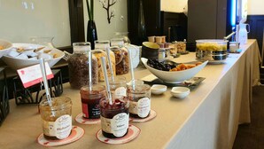 Une table de buffet proposant divers plats et accompagnements, notamment des pots de confitures et un saladier de fruits.