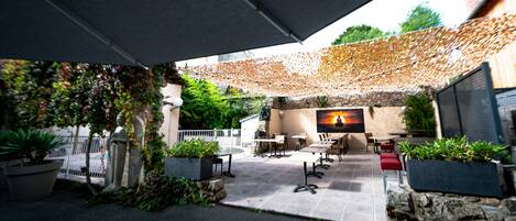 Un patio al aire libre con suelo de piedra, mobiliario exterior y una pantalla de televisión mostrando un atardecer.