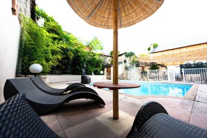 Un área junto a la piscina con sillones de descanso, una pequeña mesa y una estatua.