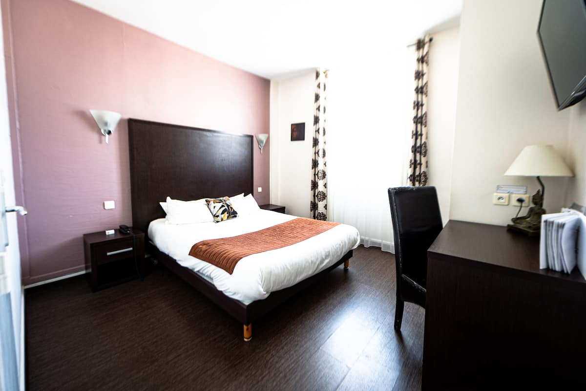 Une chambre d’hôtel avec un lit, un bureau, une chaise, une table de chevet et un téléviseur.