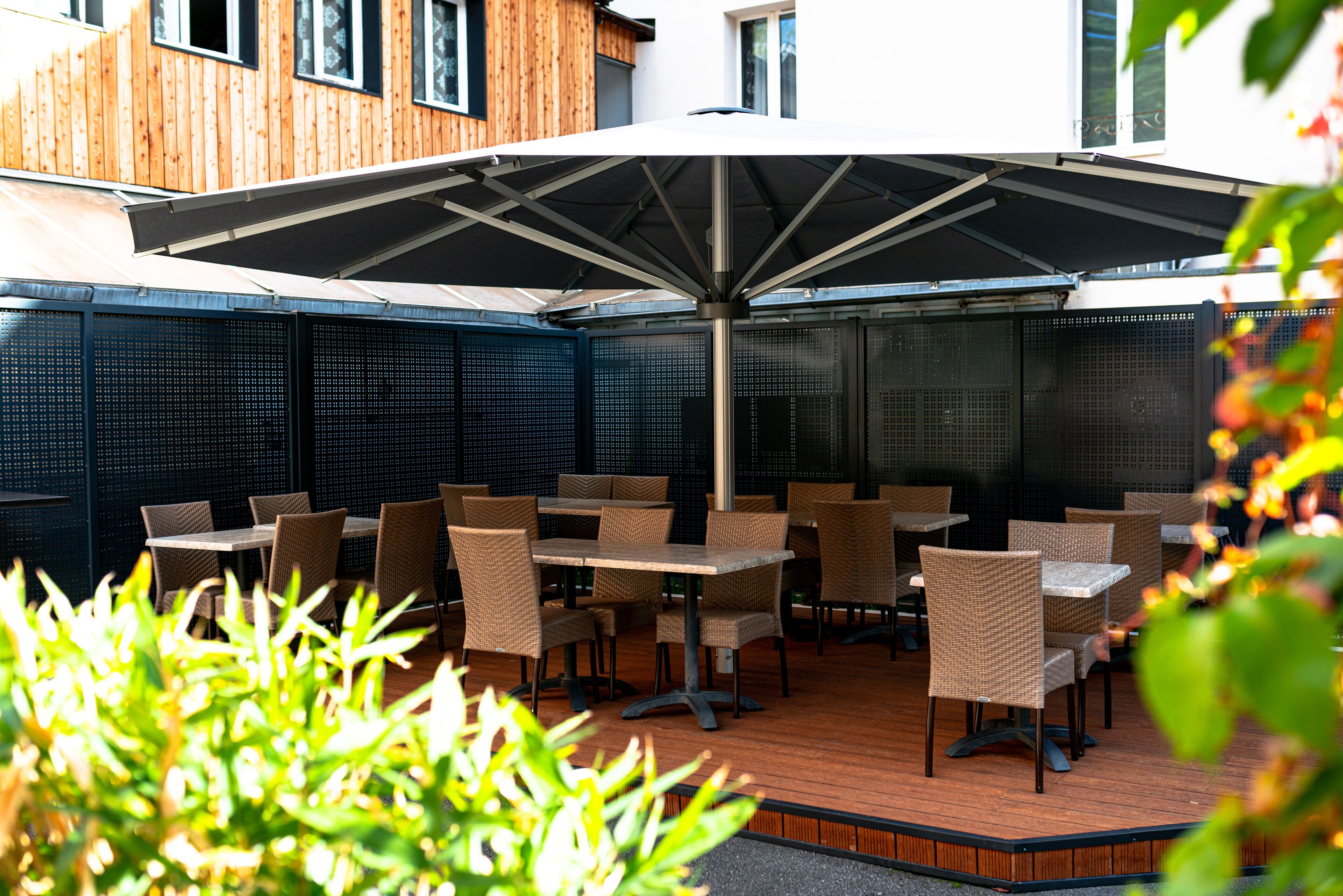 An outdoor patio with tables and chairs, a large umbrella, and a wooden wall.