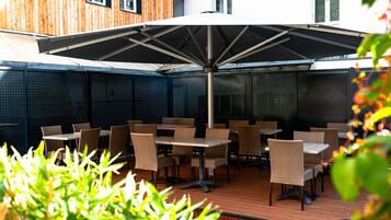 Eine Terrasse im Freien mit Tischen, Stühlen und einem großen Sonnenschirm, an einer Holzverkleidung.