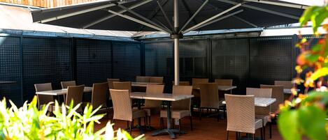 An outdoor patio with tables and chairs, a large umbrella, and a wooden wall.
