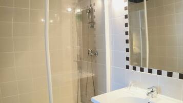 Un baño moderno con ducha de vidrio, lavamanos blanco y espejo con detalle de mosaico blanco y negro.