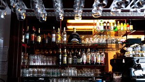 Un bar avec des étagères remplies de bouteilles d’alcool et de verres, un appareil à café et un menu affiché au mur.