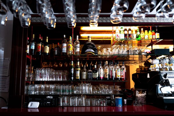 Un bar avec des étagères remplies de bouteilles d’alcool et de verres, un appareil à café et un menu affiché au mur.