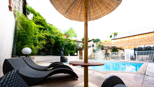 Un espace aménagé au bord de la piscine, avec des chaises longues et une table placée sous un auvent.