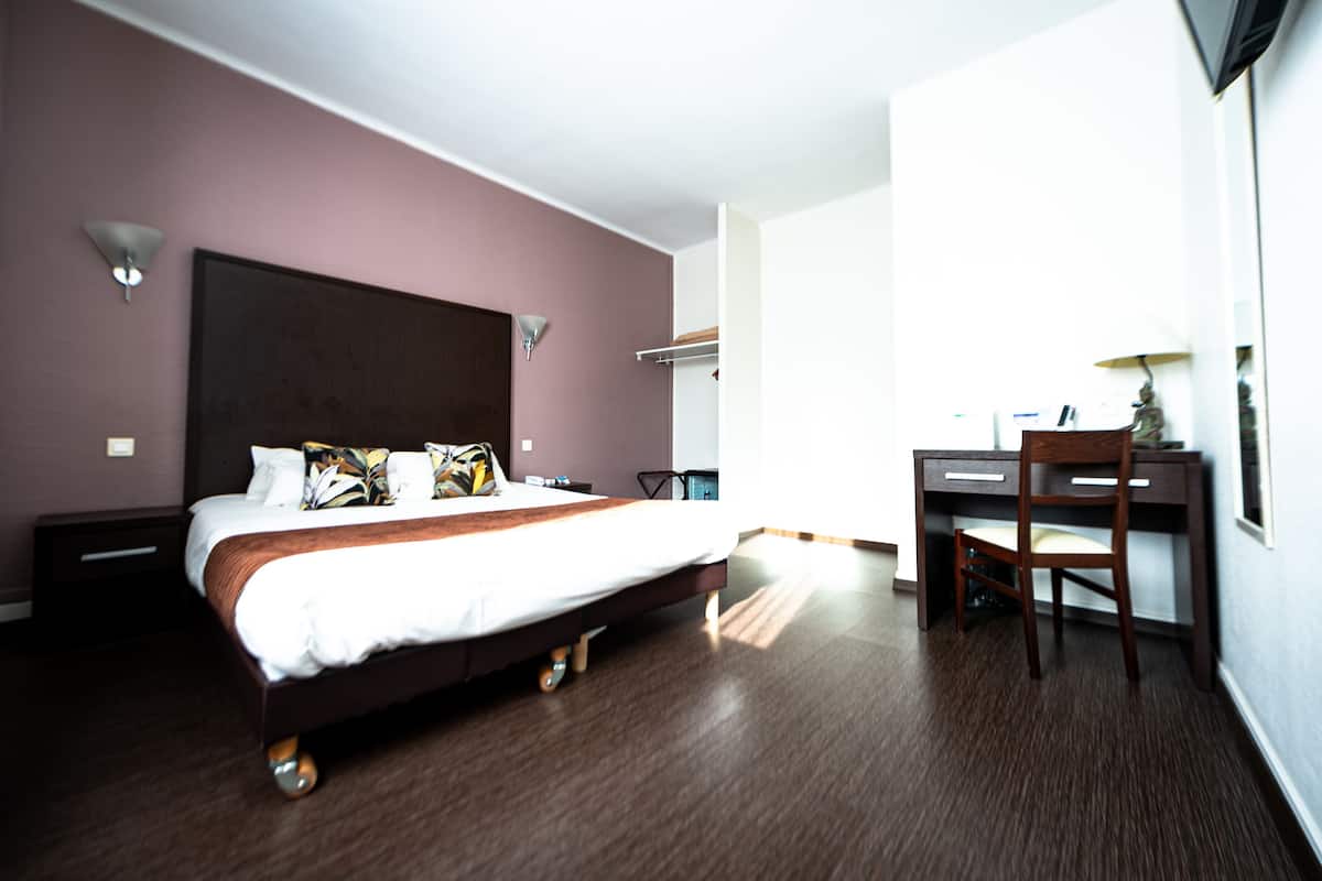 Une chambre d’hôtel équipée d’un lit, d’un bureau, d’une chaise et d’un téléviseur fixé au mur.