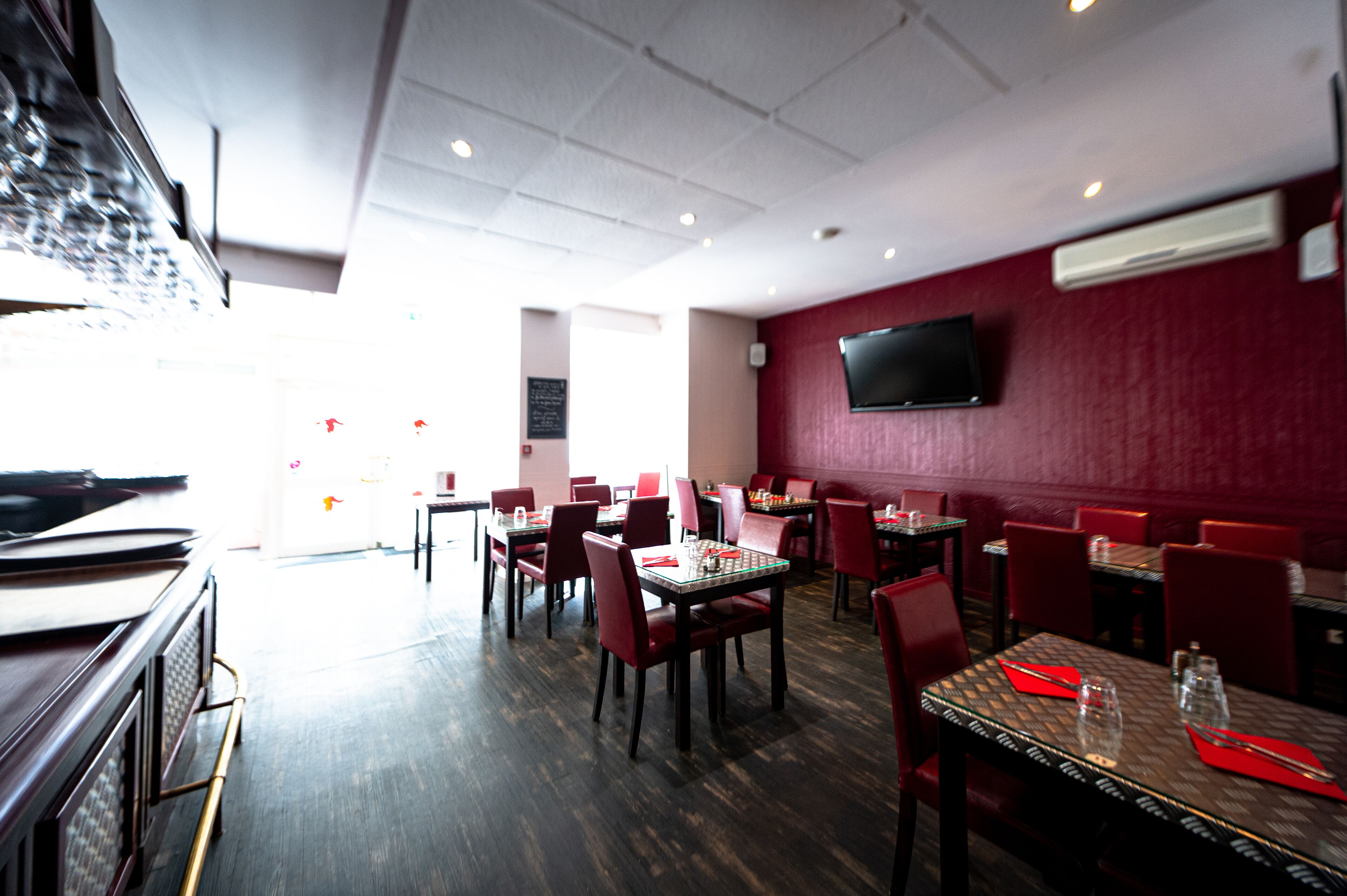Een restaurant met rode stoelen, tafels en een flatscreen aan de muur.