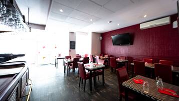 Een restaurant met rode stoelen, tafels en een flatscreen aan de muur.
