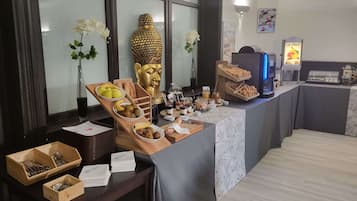 A breakfast buffet setup with various food items and a Buddha statue.