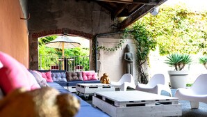 Un espace extérieur aménagé avec des sièges, abrité par un toit, comprenant un canapé bleu, des chaises blanches et une statue.