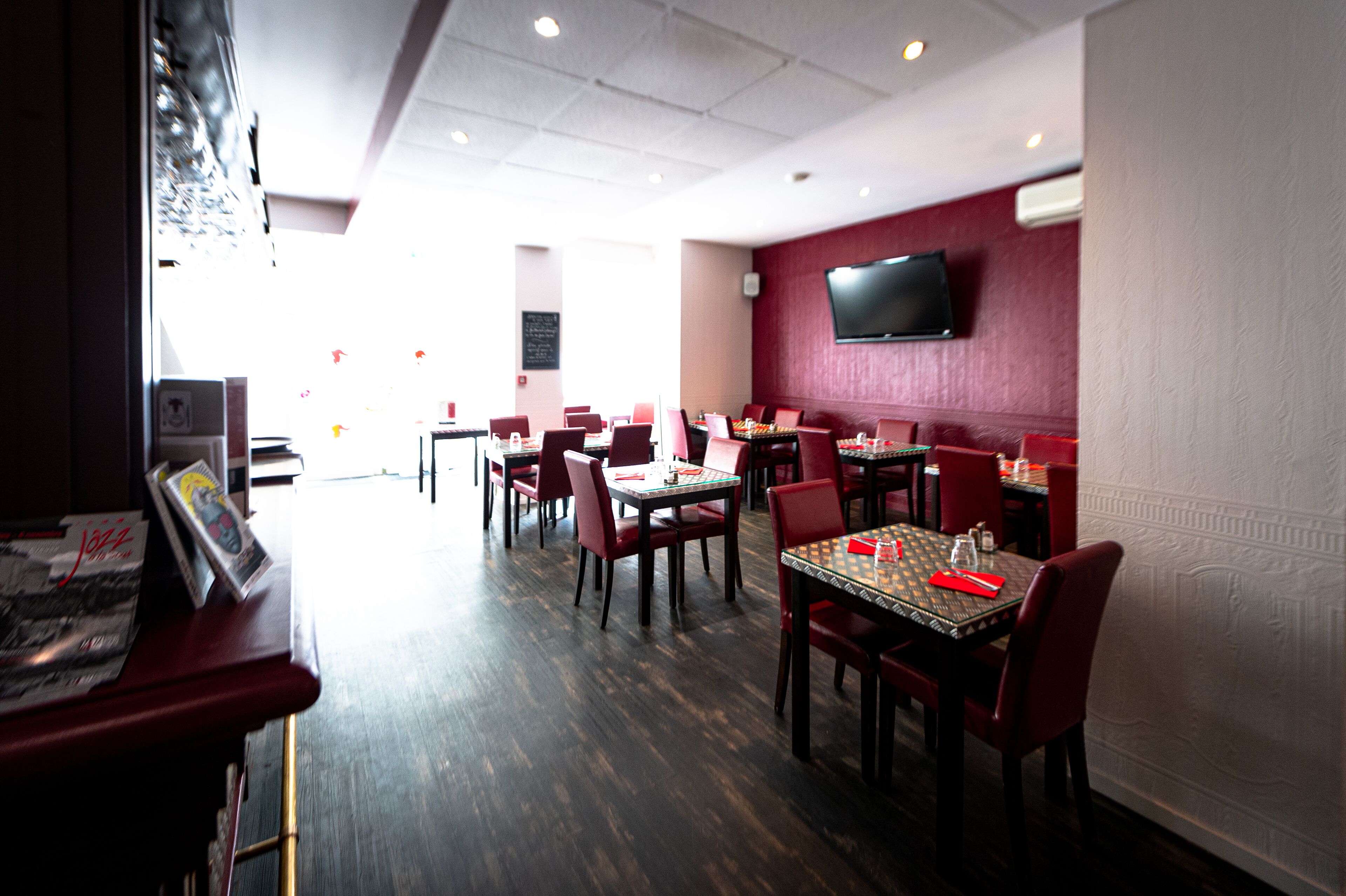 A restaurant with multiple tables and chairs, a flat-screen TV mounted on the wall, and a wooden floor.
