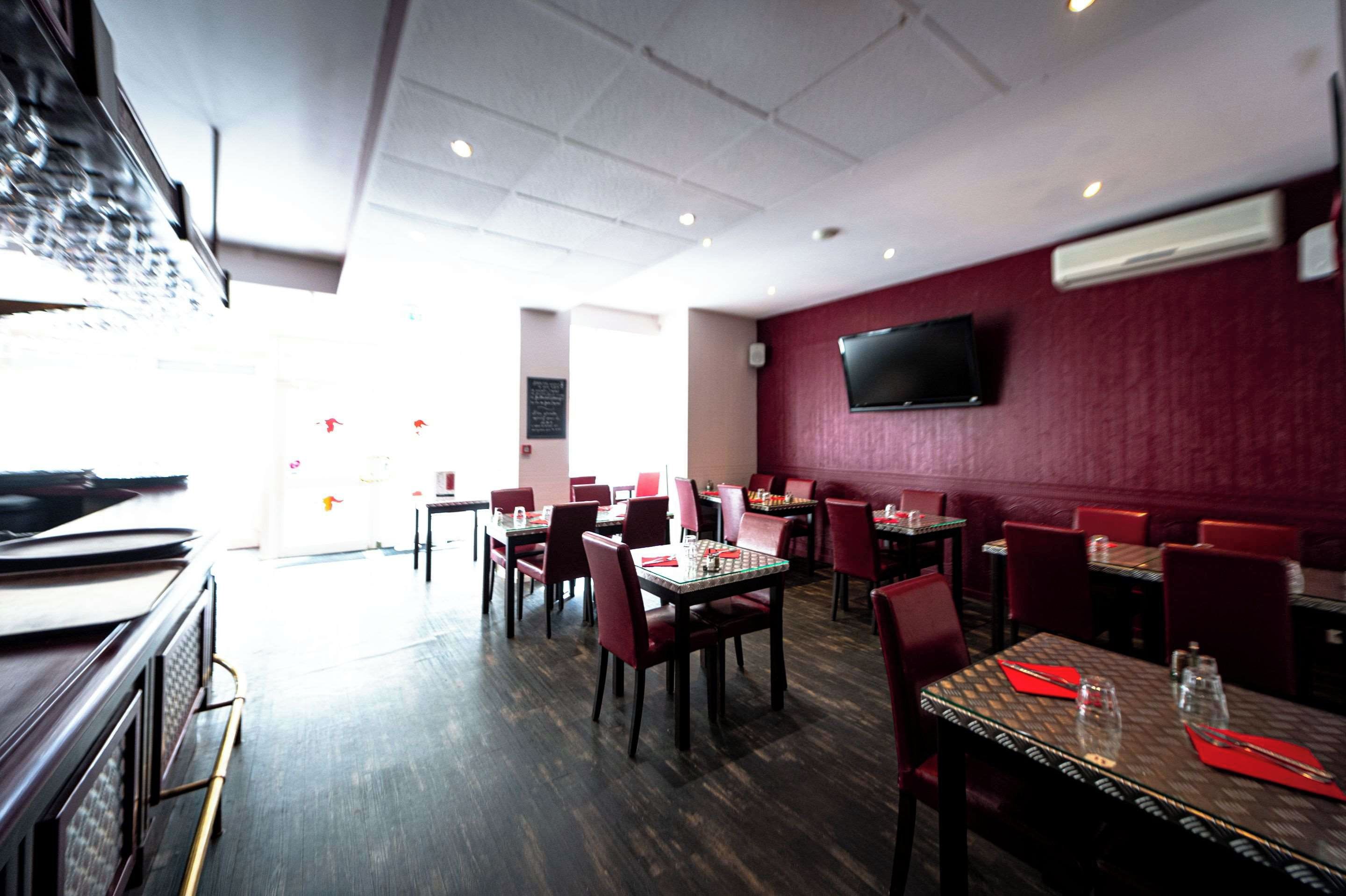 L’intérieur d’un restaurant, avec de nombreuses tables et chaises, un téléviseur à écran plat fixé au mur et une vue sur la rue.