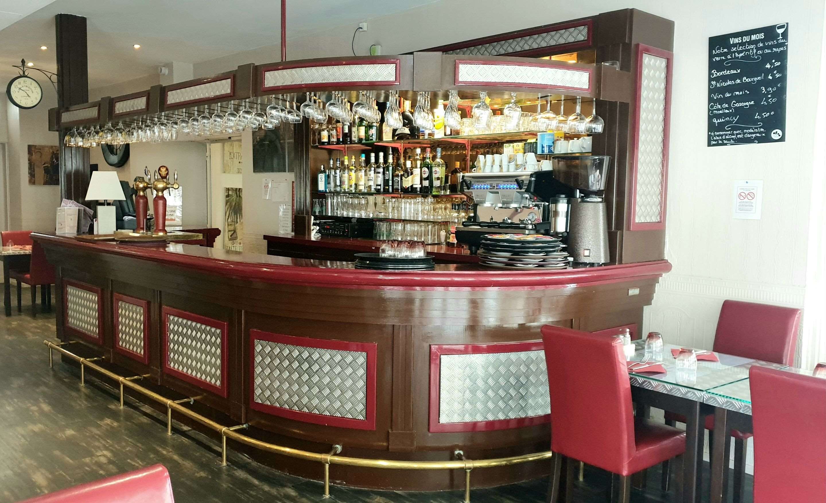 A bar area with a counter, shelves of bottles, glasses, and a coffee machine.