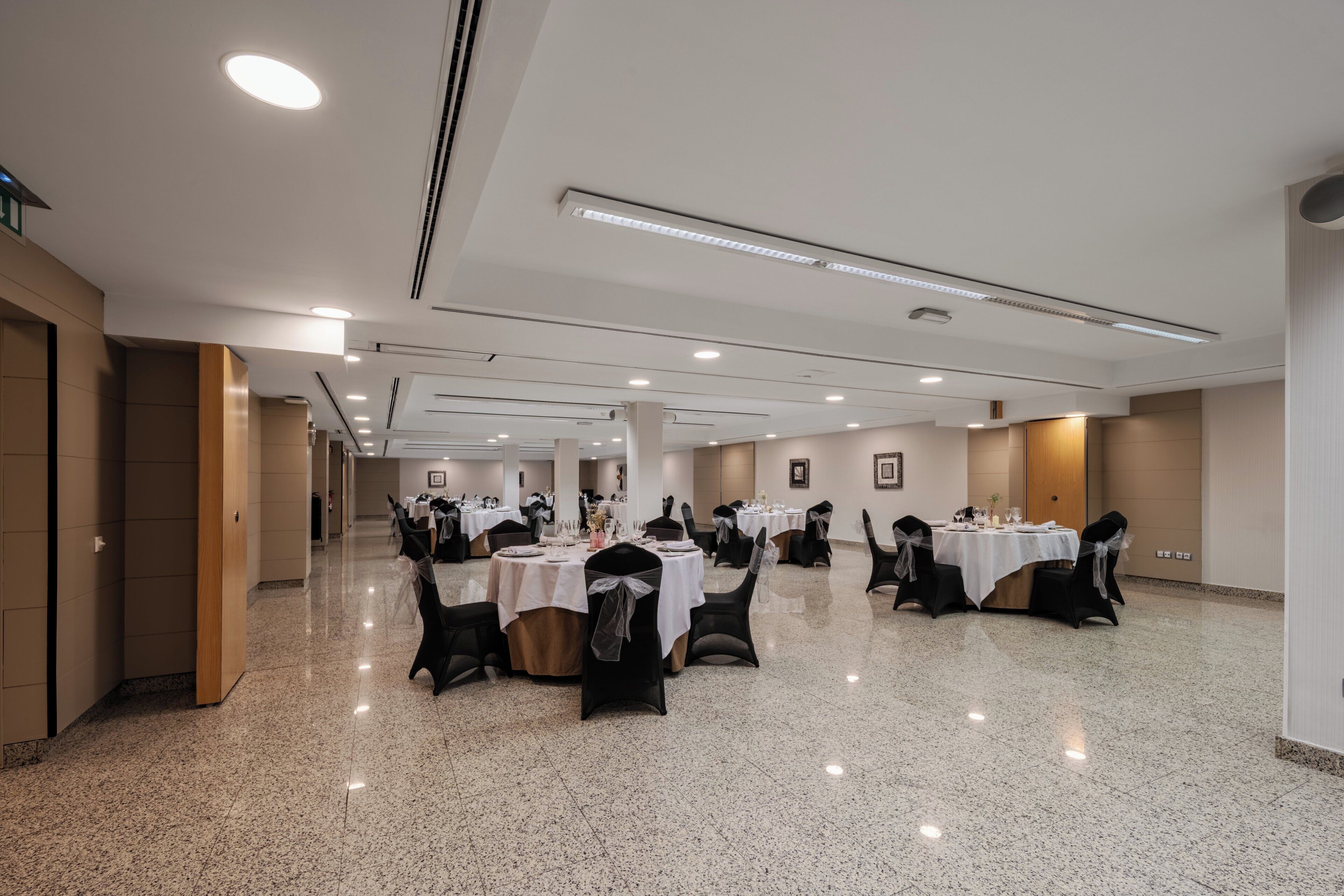 Un amplio salón de banquetes con varias mesas redondas, cada una dispuesta con sillas y manteles blancos.