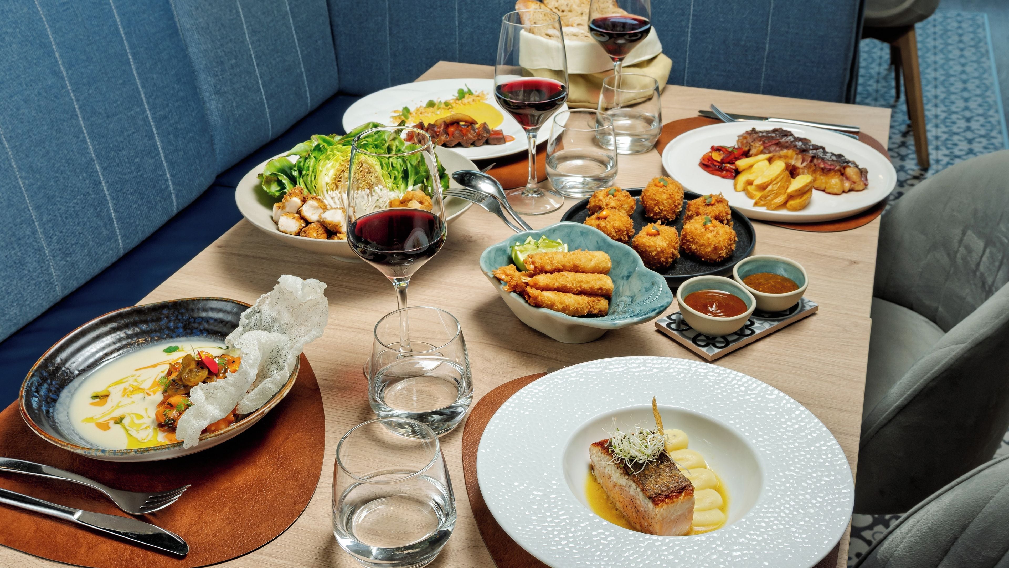 Una mesa de comedor con diversos platos, copas de vino tinto y cubiertos.