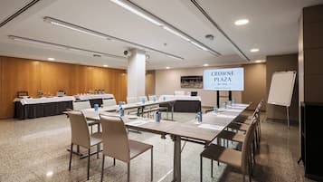 A conference room with a long table, chairs, a whiteboard, and a screen displaying 'CROWNE PLAZA BY IHG Madrid Airport'.