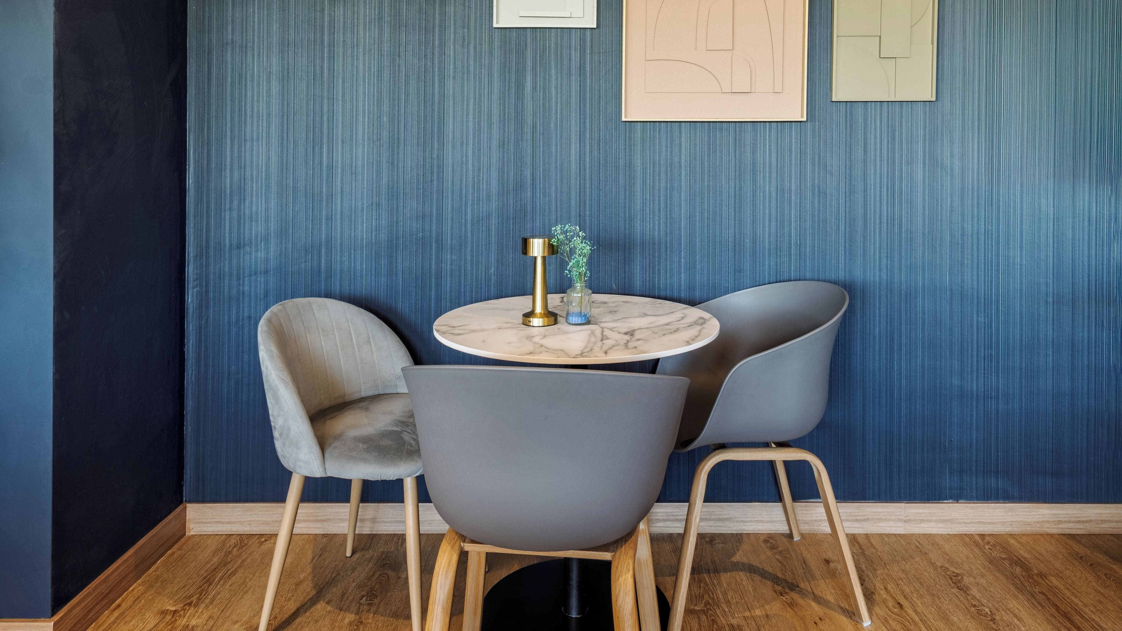 Een kamer met een ronde tafel, twee stoelen, een vaas met bloemen en een muur met kunstwerken.