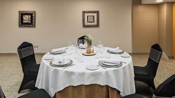 A round table set for a meal with chairs, framed artwork on the walls, and a carpeted floor.