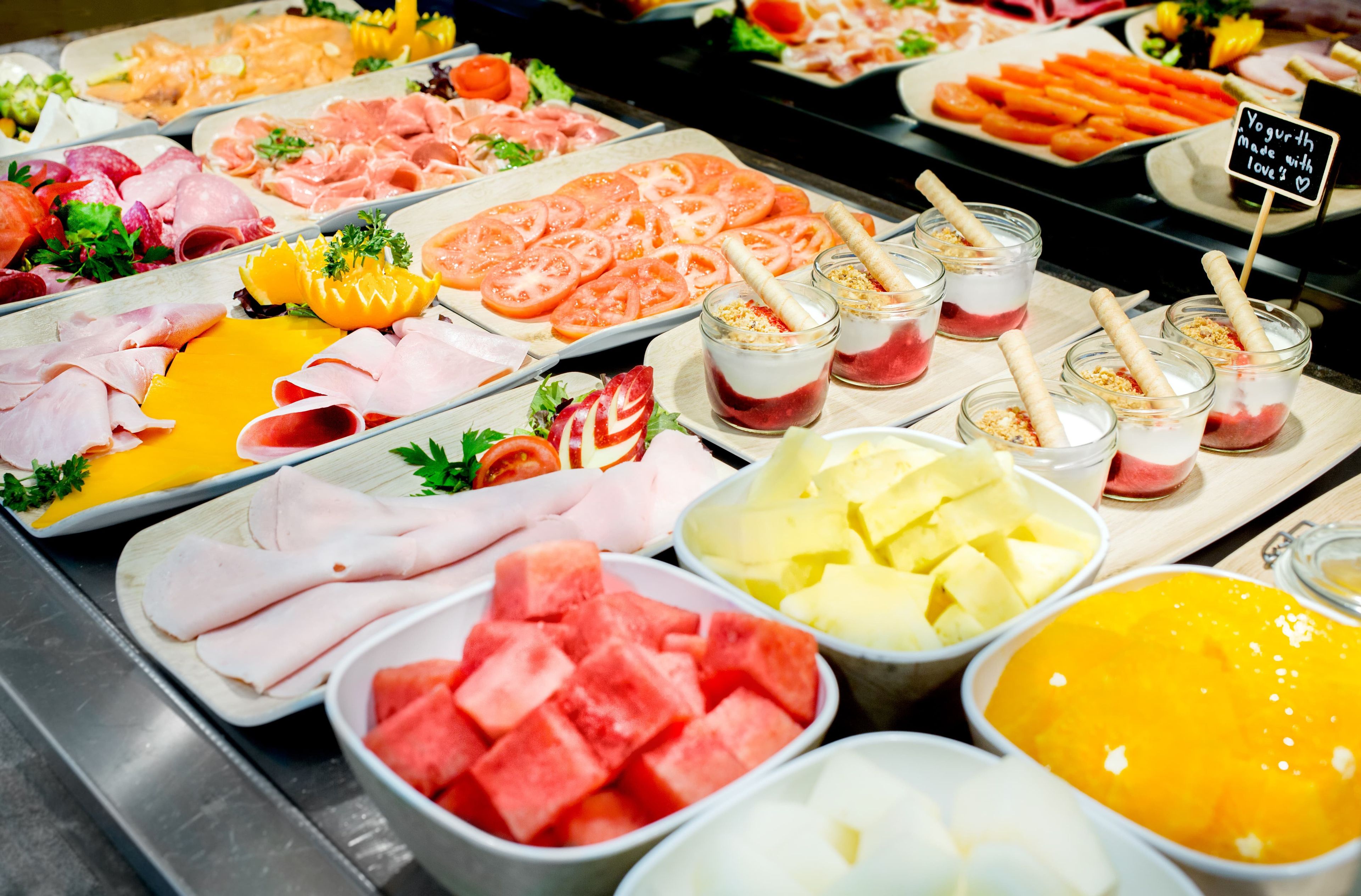 Un bufé con diversos alimentos, incluyendo carnes, quesos, frutas y postres.
