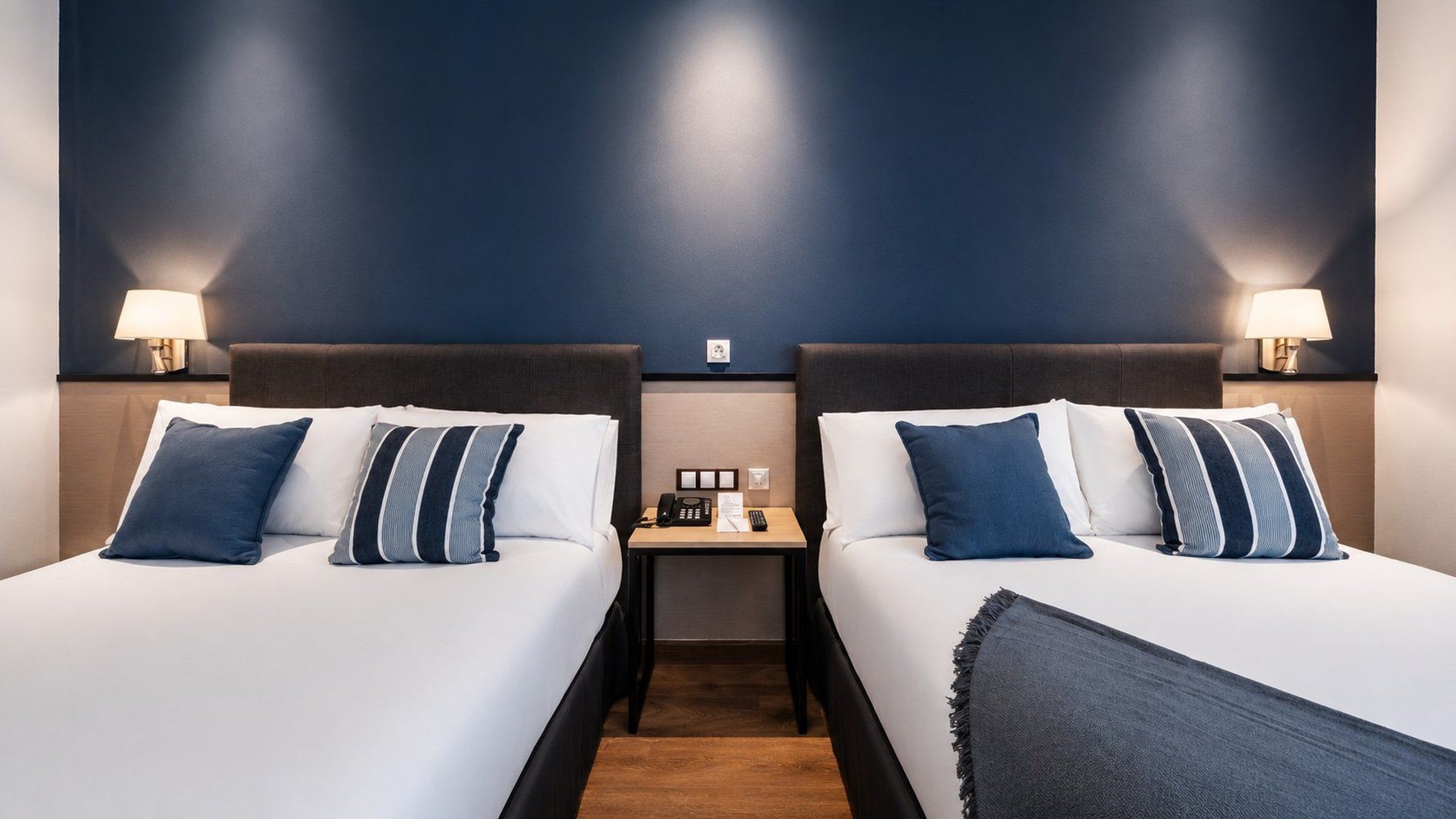 Een hotelkamer met twee bedden, een nachtkastje en wandlampen.