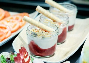 Três potes de vidro com sobremesa em camadas e palitos de wafer, dispostos numa bandeja com tomates fatiados e salada.