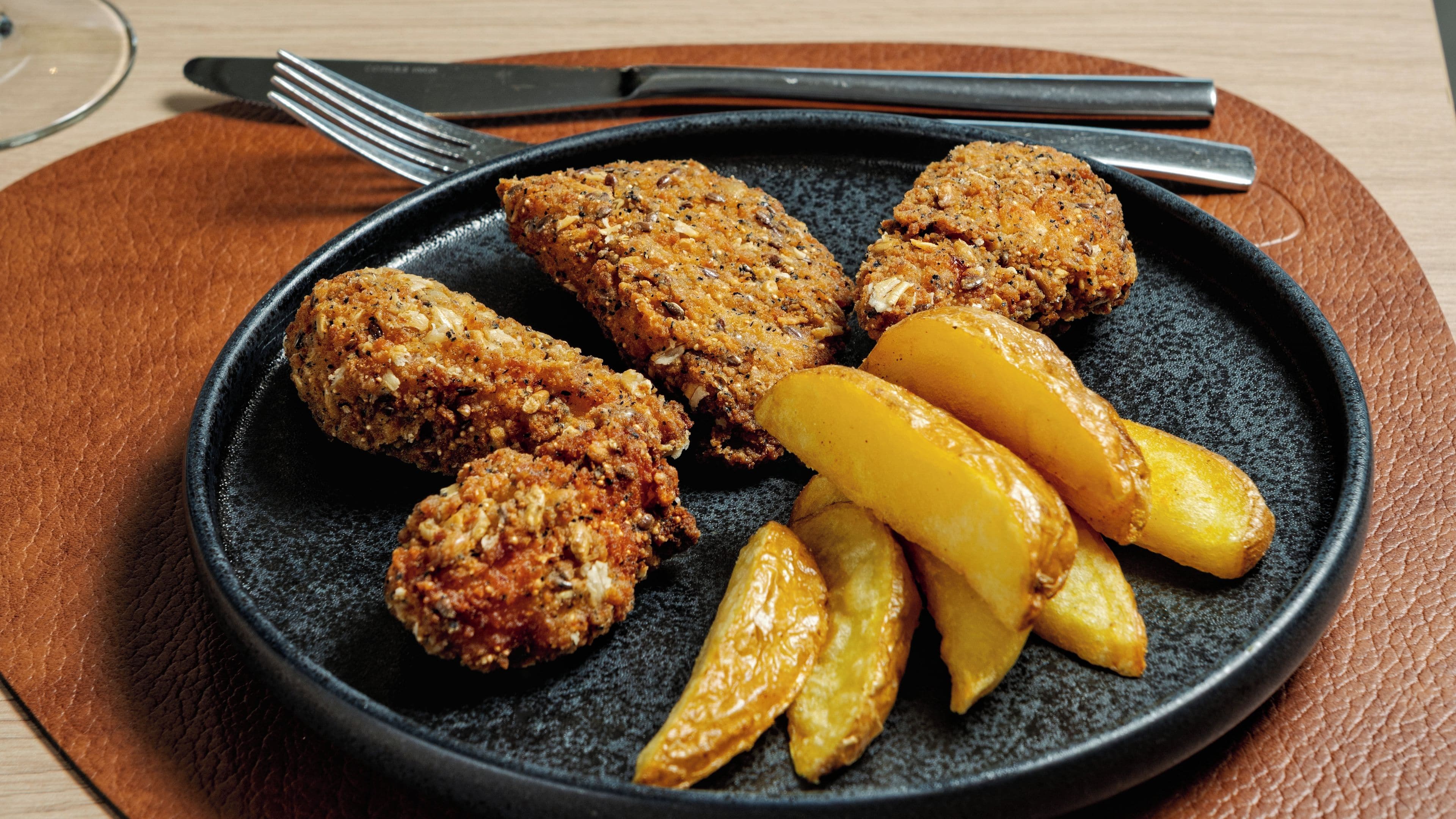 A plate with breaded chicken cutlets and golden potato wedges on a dark plate.