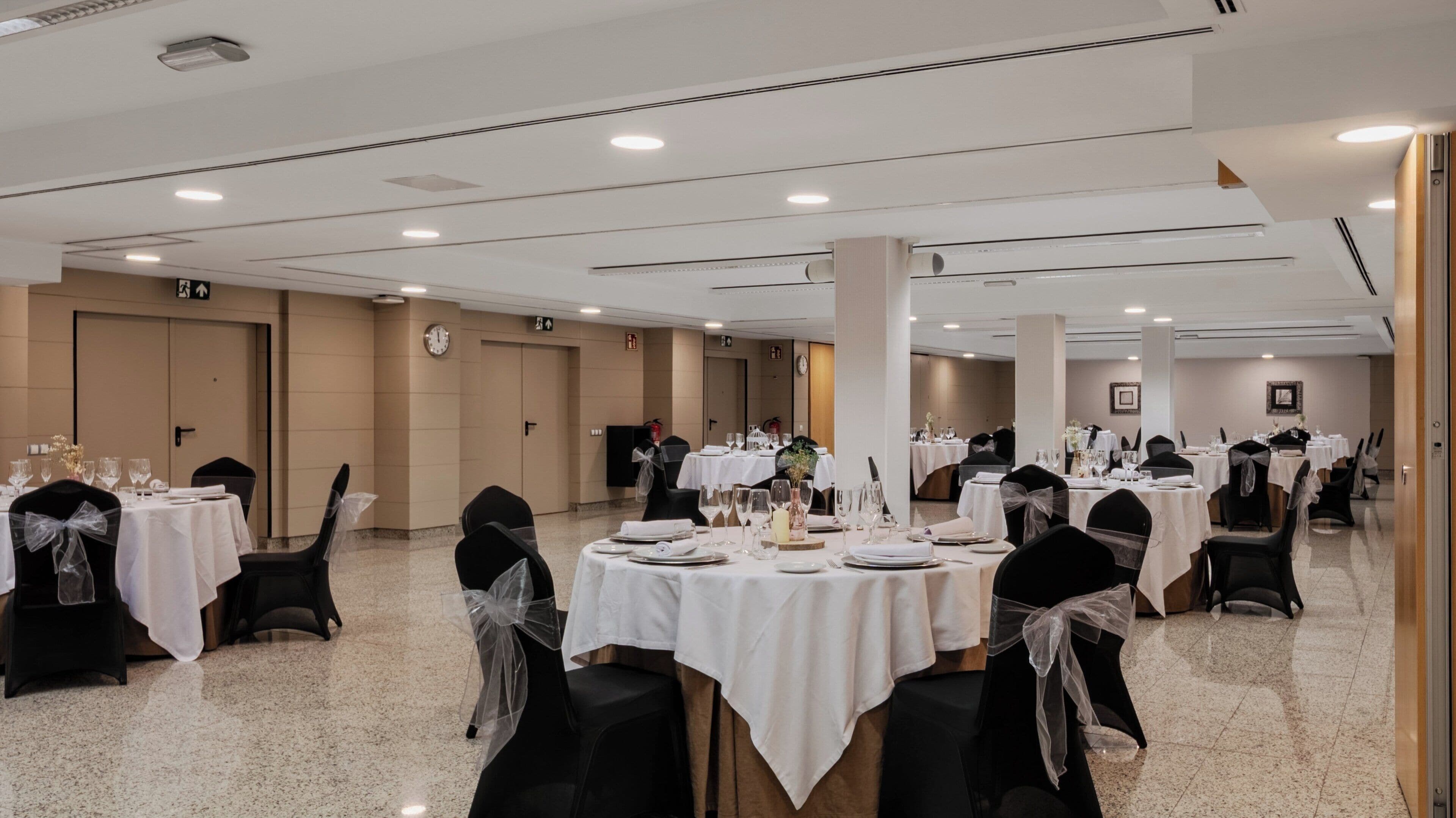 Een feestzaal met ronde tafels gedekt voor een diner, zwarte stoelen met witte kleden, en een gepolijste vloer.