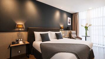A hotel room with a large bed, bedside lamps, a chair, a small table, and a vase with flowers.