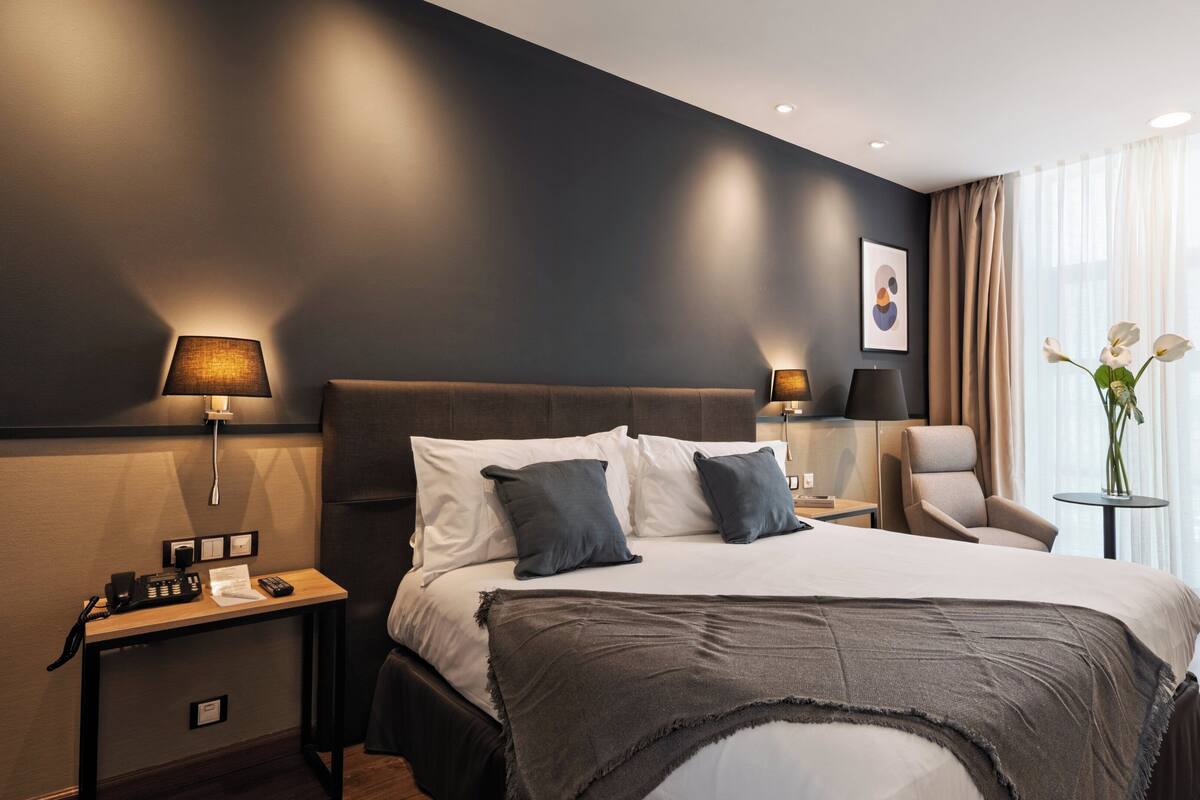 Una habitación de hotel moderna con una cama grande, lámparas de noche, un escritorio con teléfono y una silla.