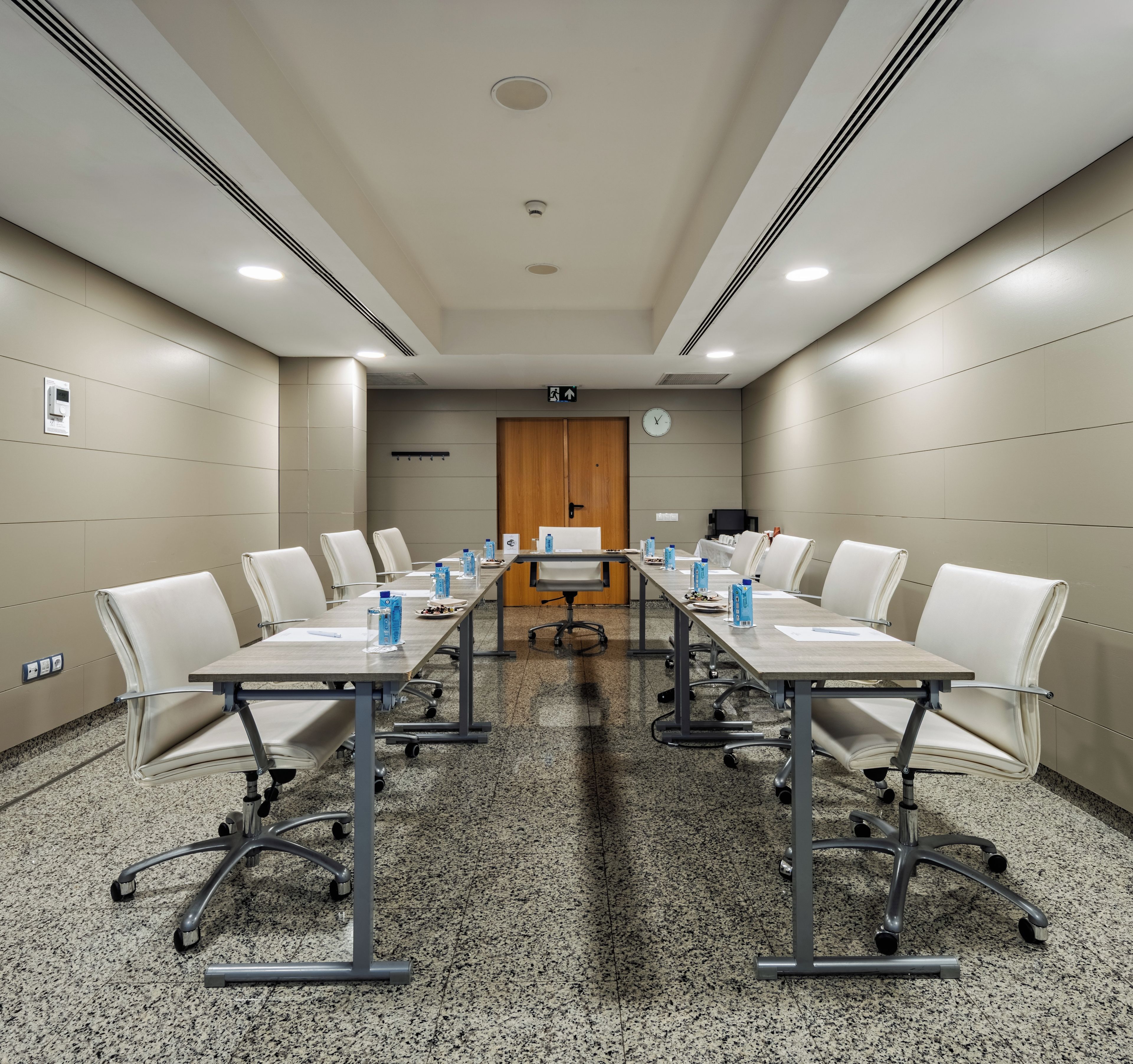 Un salón de conferencias con una mesa larga, sillas blancas y un reloj en la pared.