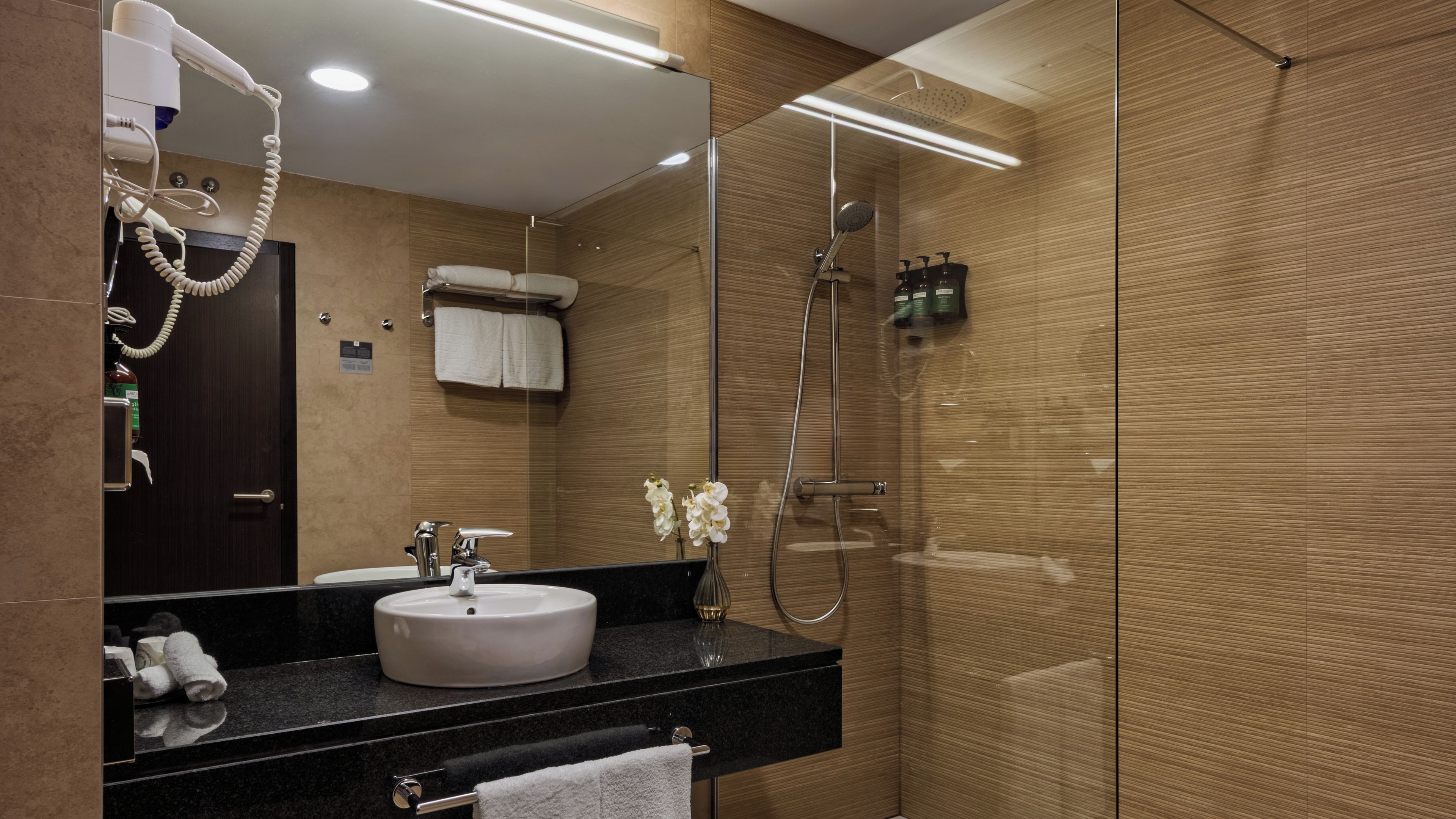 Un baño moderno con un lavabo redondo, un espejo, un secador de pelo y una ducha.