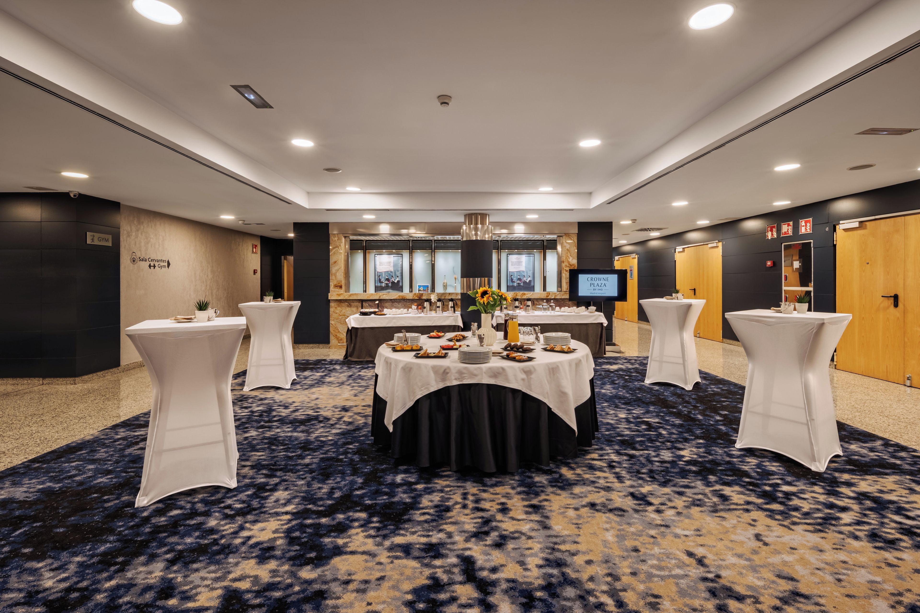A conference room with round tables, white chairs, a large screen, and a marble wall.