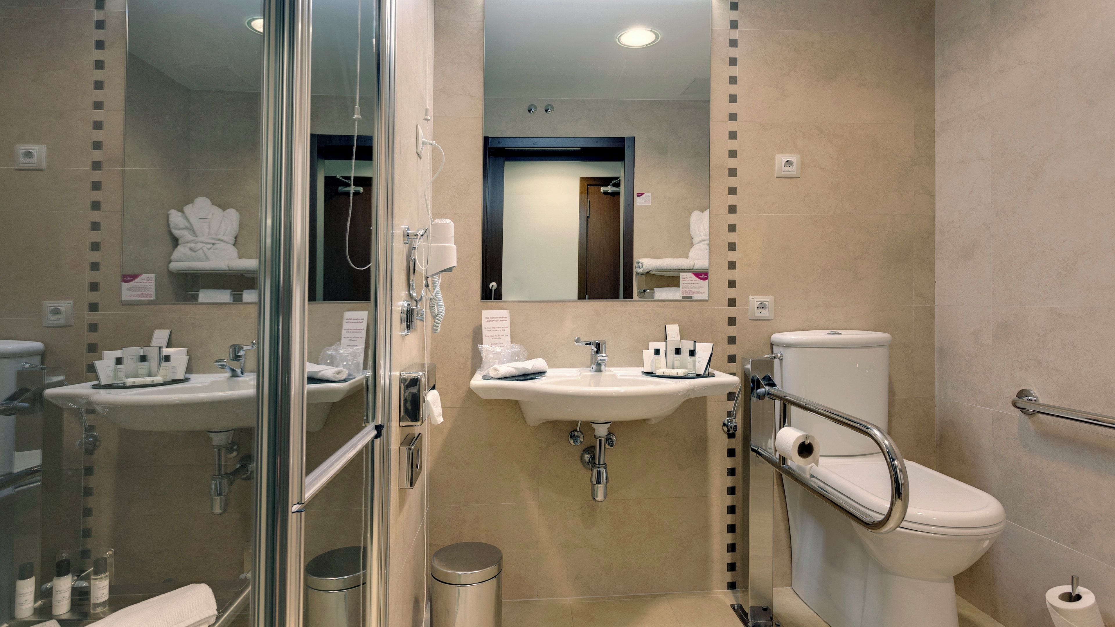 A modern bathroom with a glass-enclosed shower, two sinks, a toilet, and a hand dryer.