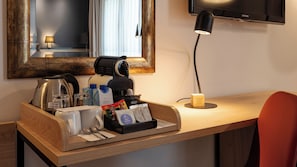 A hotel room with a wooden desk, a coffee maker, a kettle, a mirror, a TV, and a bedside lamp. - Crowne Plaza Madrid Airport by IHG (Madrid)